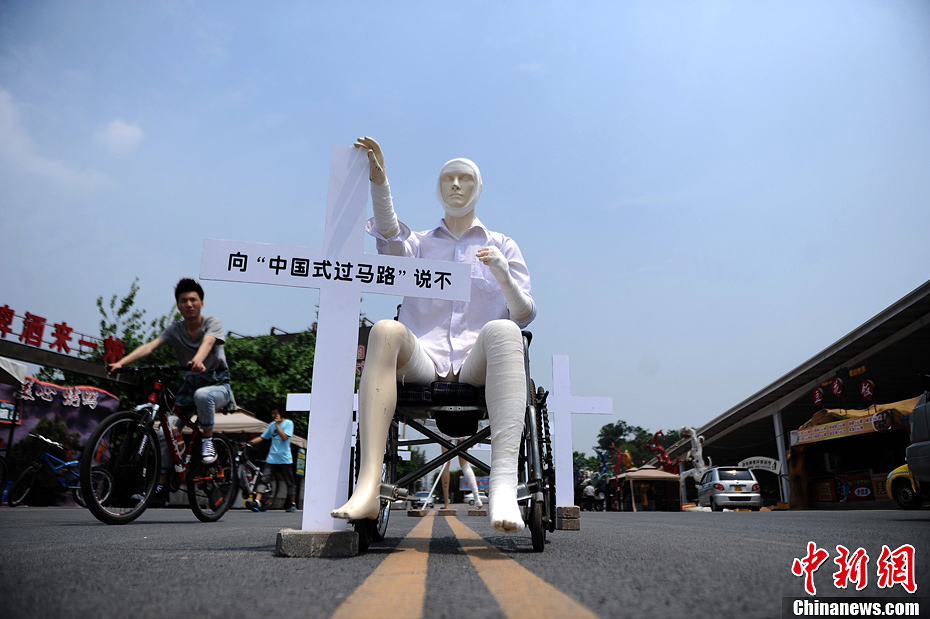 4月16日，重慶市洋人街上擺放著兩個受了傷的塑料人像“模特”，旁邊十字架上寫著向“中國式過馬路”說不