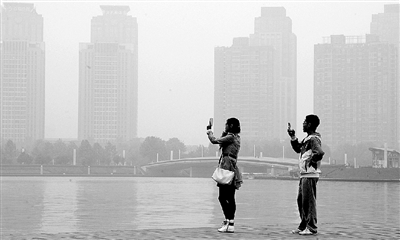 29日中午，鄭東新區(qū)如意湖畔，兩個年輕人拍攝霧霾中的景色。 鄭州晚報記者 馬健 圖