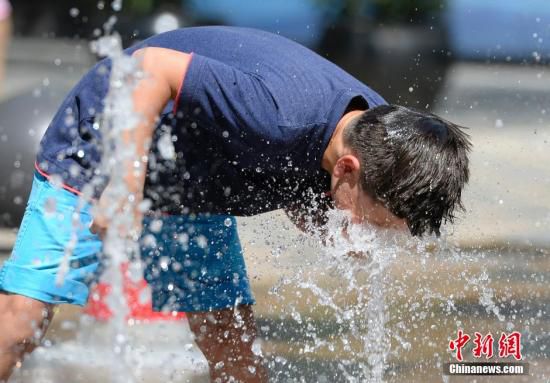 5月29日，一名小孩將頭伸向北京街頭的噴泉以降溫祛暑。