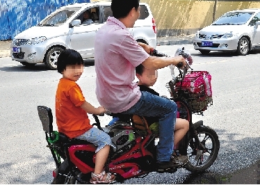 周先生騎著一輛低矮的電動車帶著一對兒女，很不安全。
