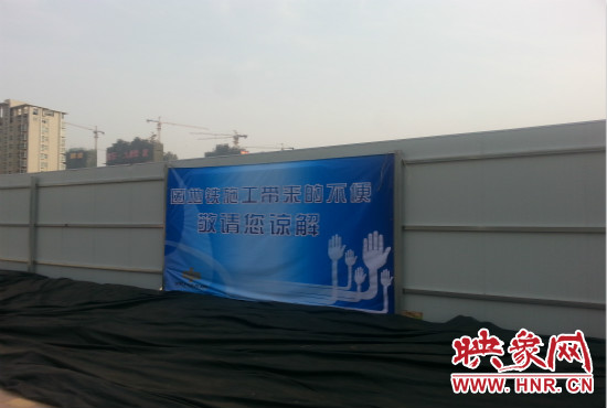 道路南側(cè)圍起了白色的圍擋，墻上標(biāo)示著“因地鐵施工帶來(lái)的不便敬請(qǐng)您諒解”的提示牌。