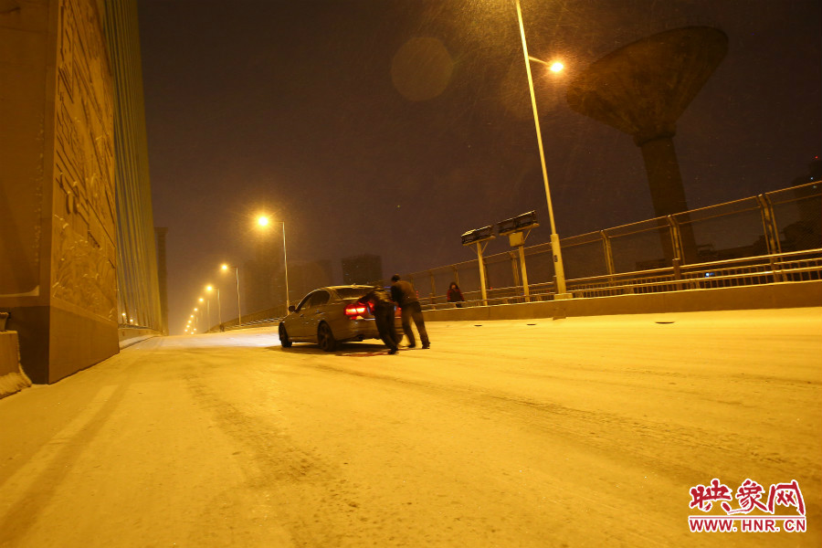 雪天路滑，汽車(chē)上橋打滑，兩名“推車(chē)人”幫助一輛私家車(chē)上坡。