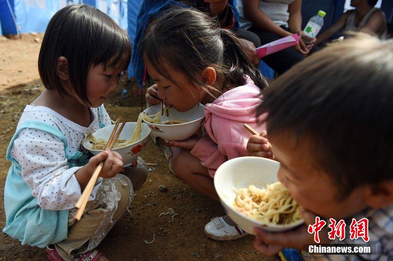 2014年8月6日，云南魯?shù)辇堫^山災(zāi)區(qū)，兒童在帳篷外吃飯。
