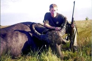 哈里王子手持獵槍，蹲在一頭遭到獵殺的水牛旁邊