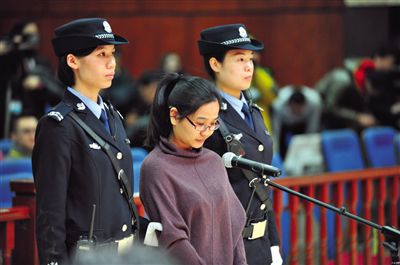 被告人盧梅低著頭，站在朝陽法院刑事審判庭的被告席上。