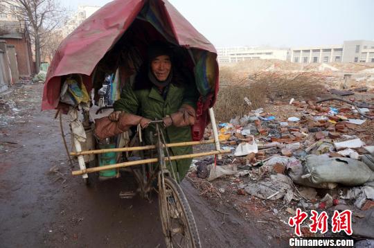 圖為老人走出窩棚，推著三輪車準(zhǔn)備出去撿拾廢品。周小云 攝